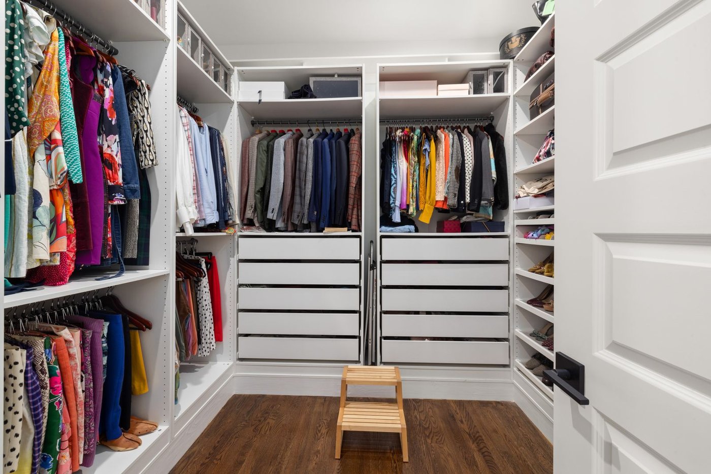 A bright, organized walk-in closet with neatly hung clothes and labeled drawers.