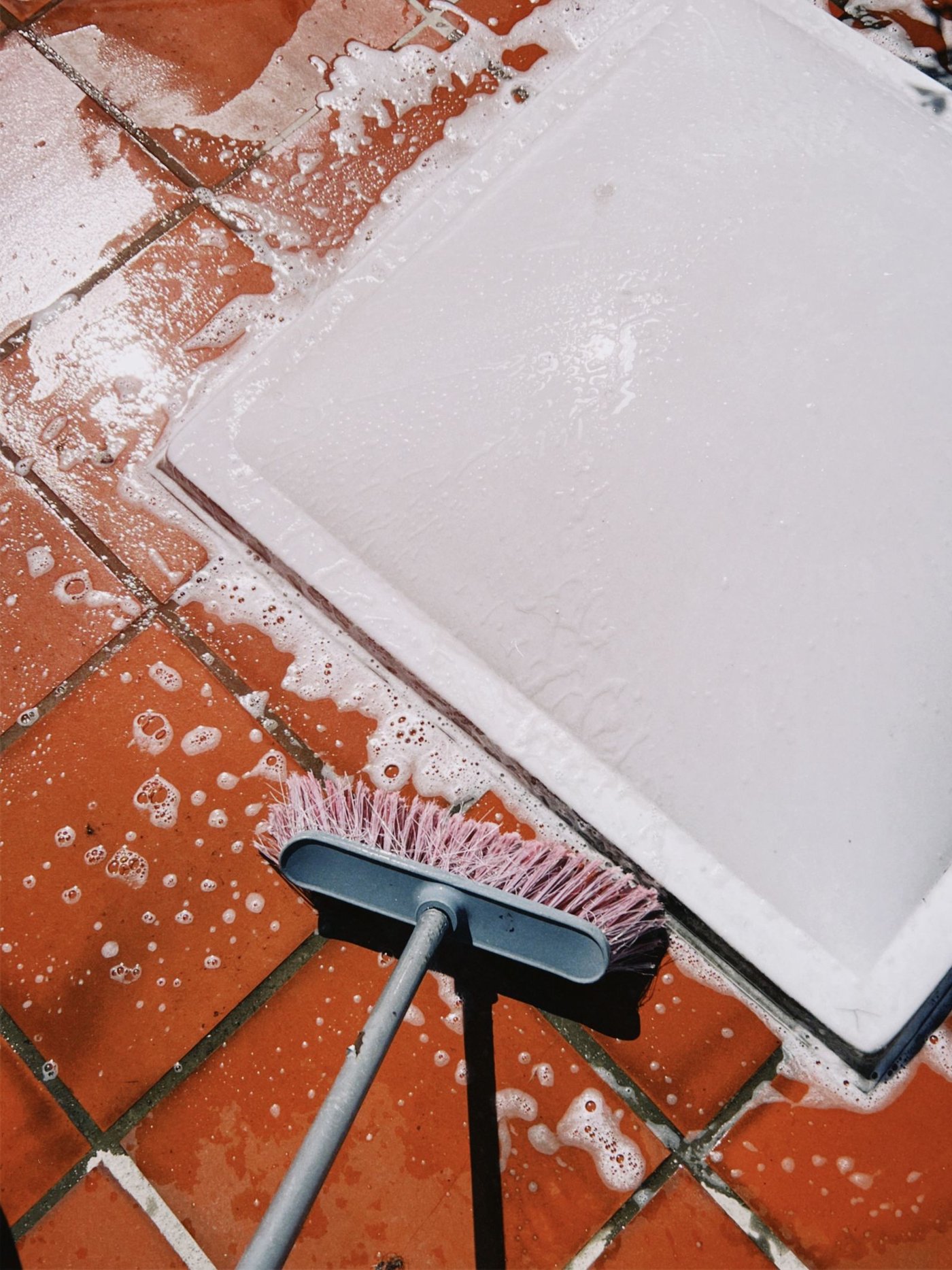 A scrub brush thoroughly cleaning a tiled floor during a fall deep clean.