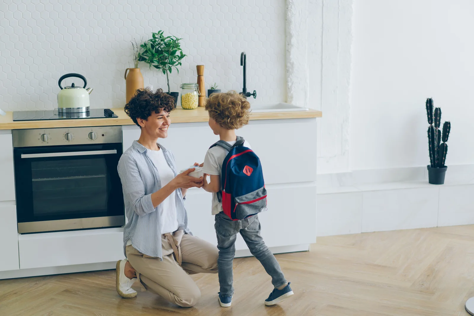 Mother and school-age child with a backpack in a bright organized kitchen before school