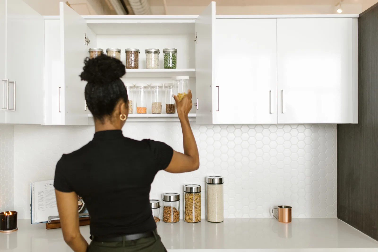 Woman arranging food storage jars on pantry shelves in a modern kitchen